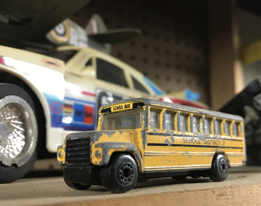 Battered Matchbox school bus with a racing Porsche behind it.