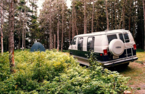 A 1984 Dodge B-250 Conversion Van in the woods with a tent.