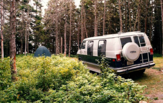 A 1984 Dodge B-250 Conversion Van in the woods with a tent.