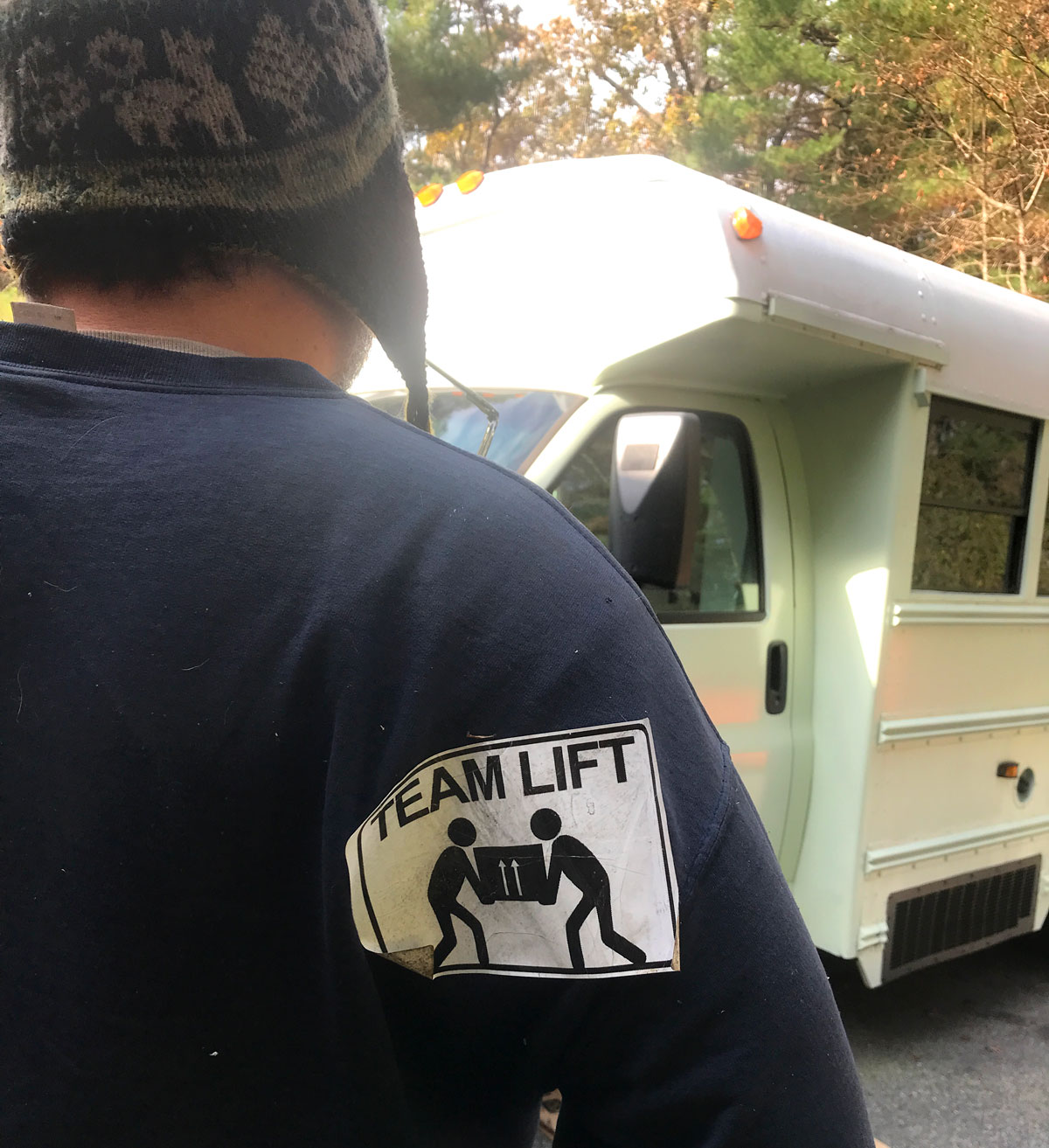 Co-owner Kris looking at bus with a Team Lift sticker on this shirt.